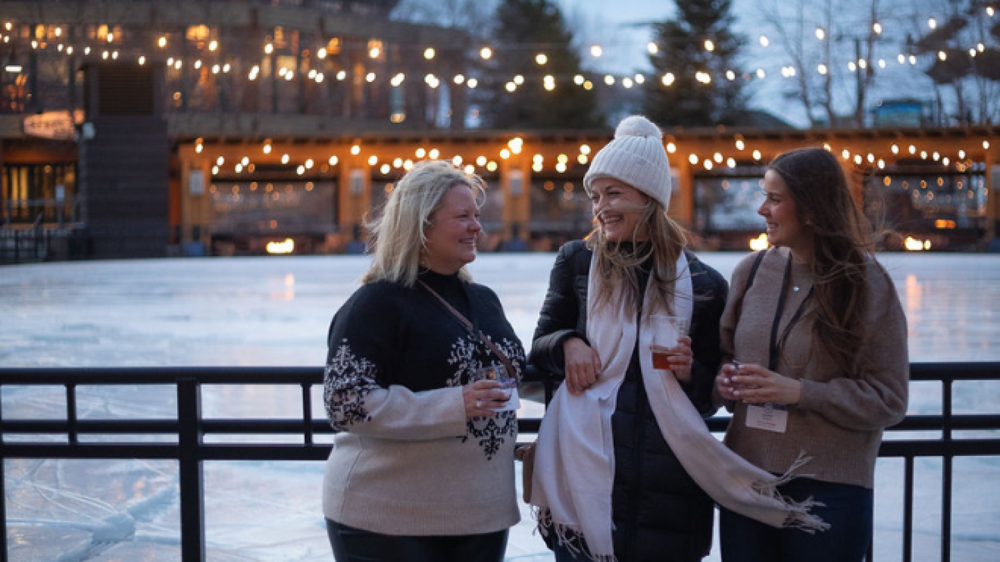 A group of women laughs in front of an outdoor ice rink